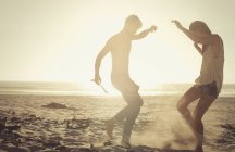 Couple ludique dansant sur la plage ensoleillée au coucher du soleil — Photo de stock