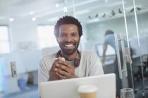 Retrato sorridente, empresário criativo confiante usando telefone inteligente no laptop no escritório — Fotografia de Stock