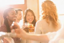 Smiling women friends toasting beer glasses in sunny bar — Stock Photo