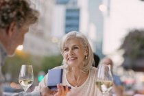 Smiling senior woman receiving jewelry gift from husband at urban sidewalk cafe — Stock Photo