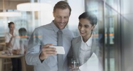Lächelnder Geschäftsmann und Geschäftsfrau beim Ansehen von Videos auf dem Smartphone im Büro — Stockfoto