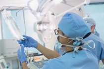 Anestesióloga femenina preparando goteo IV en quirófano - foto de stock