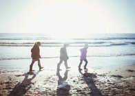 Hermano y hermanas en ropa de abrigo caminando en arena mojada en la playa soleada - foto de stock