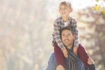 Smiling father carrying son on shoulders outdoors — Stock Photo