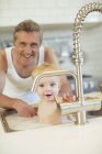 Father bathing baby in kitchen sink — Stock Photo