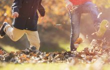 Imagen recortada de niños juguetones patadas hojas de otoño - foto de stock