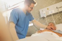 Krankenpfleger mit Stethoskop auf Patientin im Krankenhausbett — Stockfoto