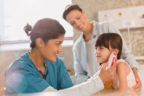 Female nurse using digital thermometer in ear of girl patient in examination room — Stock Photo