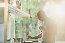 Homem maduro bebendo vinho branco e cozinhar no fogão na cozinha ensolarada — Fotografia de Stock