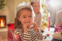 Menina retrato no papel de Natal coroa segurando favor festa na mesa de jantar de Natal — Fotografia de Stock