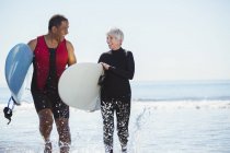 Happy senior couple with surfboards on beach — Stock Photo