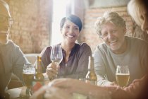 Parejas riéndose bebiendo vino blanco y cerveza en la mesa del restaurante - foto de stock