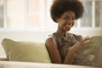 Femme utilisant une tablette numérique sur le canapé et regardant la caméra — Photo de stock
