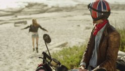 Молодий чоловік на мотоциклі дивиться, як жінка біжить на пляж — стокове фото