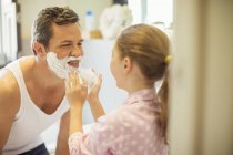 Chica frotando crema de afeitar en la cara del padre - foto de stock