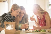 Teenage girls eating sushi and texting with cell phone in sunny kitchen — Stock Photo