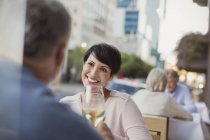 Smiling couple toasting white wine glasses at urban sidewalk cafe — Stock Photo