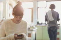Junge Frau textet mit Handy in Küche — Stockfoto
