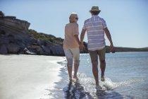 Couple holding hands walking along shore — Stock Photo