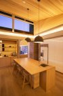 Techo de madera inclinado iluminado y luces colgantes sobre isla de cocina - foto de stock