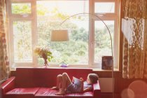 Мальчик читает, используя цифровую табличку на диване в гостиной — стоковое фото
