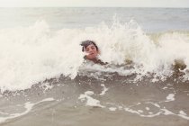 Waves splashing around boy swimming in summer ocean — Stock Photo