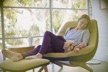 Femme avec ordinateur portable relaxant et chien caressant sur chaise — Photo de stock