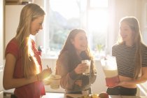 Teenage girls making smoothie in sunny kitchen — Stock Photo