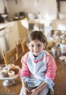 Young girl sitting on kitchen table near cupcakes — Stock Photo