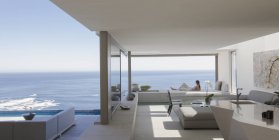 Donna che si rilassa sul moderno, lussuoso patio vetrina con soleggiata vista sull'oceano — Foto stock