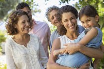Mother carrying daughter in arms with family outdoors — Stock Photo