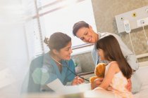 Smiling female nurse using stethoscope on girl patient in hospital room — Stock Photo