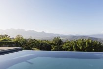 Транквіль розкішний нескінченний басейн з видом на гори під сонячним блакитним небом — стокове фото