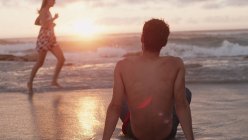 Jovem assistindo mulher correndo no oceano surfar ao pôr do sol — Fotografia de Stock