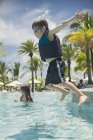 Menino pulando na piscina tropical ensolarada — Fotografia de Stock