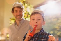 Portrait boy wearing Christmas paper crown blowing party favor — Stock Photo