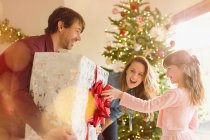 Eltern schenken Tochter in der Nähe des Weihnachtsbaums großes Weihnachtsgeschenk — Stockfoto