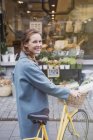 Портрет усміхненої жінки, що йде на велосипеді на міській стороні магазину — стокове фото