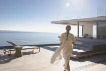 Femme marchant sur ensoleillé moderne, maison de luxe vitrine patio extérieur avec vue sur l'océan — Photo de stock