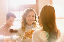 Mulheres sorridentes amigos brindar copos de cerveja no bar ensolarado — Fotografia de Stock