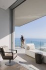 Coppia godendo di soleggiata vista sull'oceano dal balcone vetrina casa di lusso — Foto stock