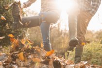 Couple in rain boots kicking autumn leaves — Stock Photo