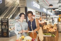 Retrato sonriente joven lesbiana pareja supermercado compras en el mercado - foto de stock