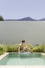 Femme assise au bord de la piscine de luxe — Photo de stock