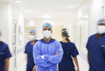 Surgeon with arms crossed, wearing scrubs standing in hospital corridor — Stock Photo