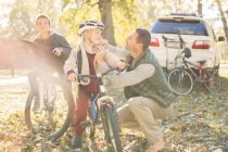 Батько кріплення шолома сина на велосипеді в осінньому лісі — стокове фото