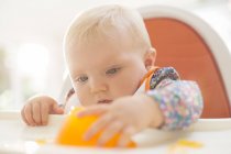 Baby girl playing with gelatin dessert in high chair — Stock Photo