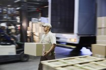 Worker carrying cardboard box at distribution warehouse loading dock — Stock Photo