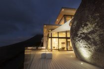 Illuminated modern house with rock feature and balcony — Stock Photo