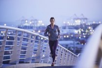 Женщина бегущая по городскому пешеходному мосту на рассвете — стоковое фото